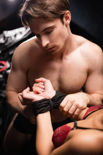 Shirtless man touching hand of girlfriend in rope and lace bra on blurred foreground on bed — Stock Photo