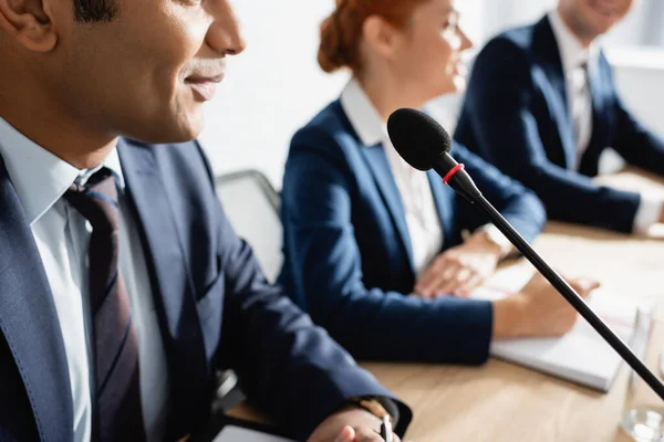 Politicien indien positif assis près du microphone avec des collègues flous sur fond — Photo de stock