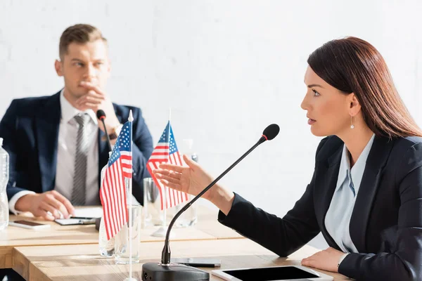 Brunette woman gesturing, while speaking in microphone, sitting near digital tablet with blurred man on background — Stock Photo