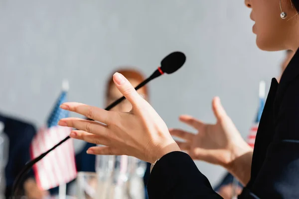 Cropped view of female politician gesturing, while speaking in microphone with blurred woman on background — Stock Photo