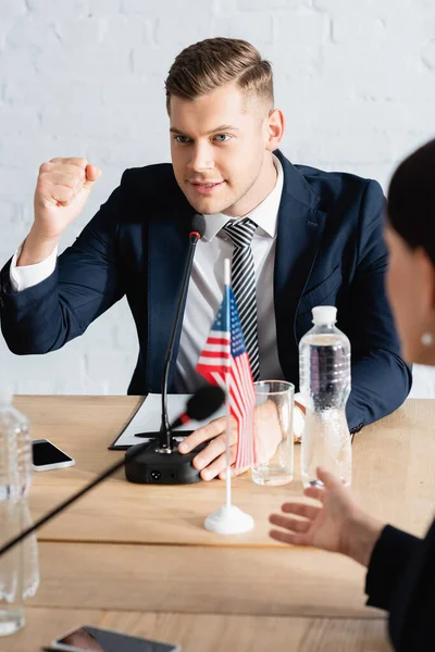 Lächelnder Politiker mit der Hand in der Luft, im Mikrofon mit verschwommener Kollegin im Vordergrund — Stockfoto