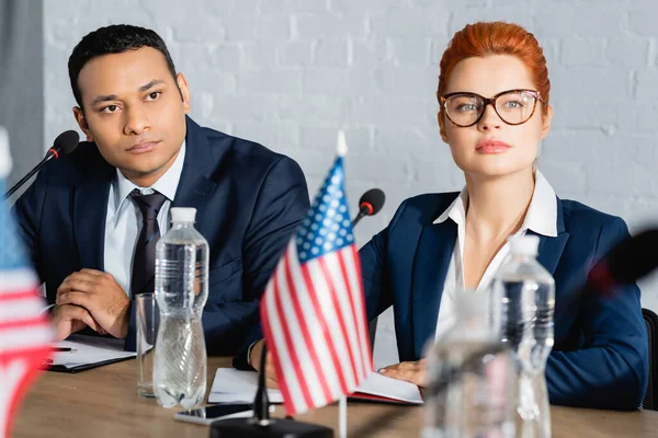 Focused interracial politicians looking away, while sitting at table during political party meeting on blurred foreground — Stock Photo