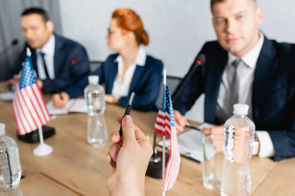 Politiker zeigt mit Stift neben Tisch im Sitzungssaal mit verschwommenen Kollegen im Hintergrund — Stockfoto