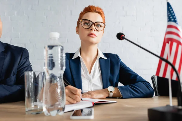 Focused woman writing in notebook, while sitting near colleague in boardroom during political party meeting — Stock Photo