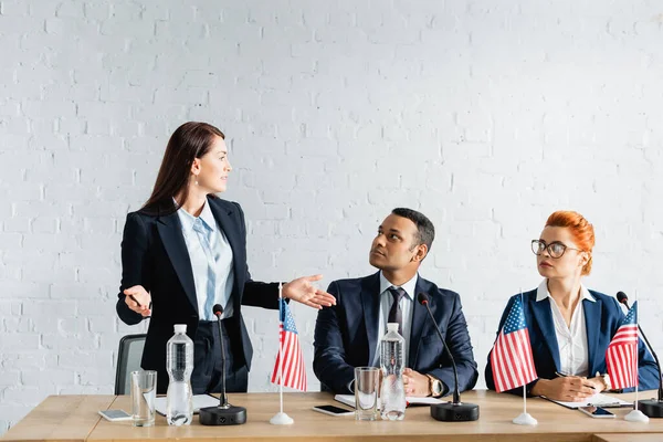 Female politician with open arms looking at interracial colleagues sitting in boardroom — Stock Photo