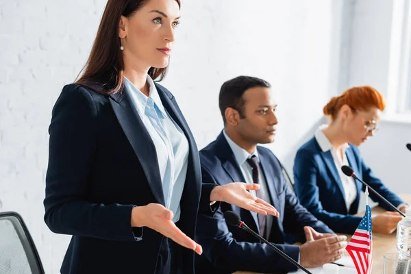 Fiducioso politico donna gesticolare e distogliere lo sguardo in sala riunioni su sfondo sfocato — Foto stock