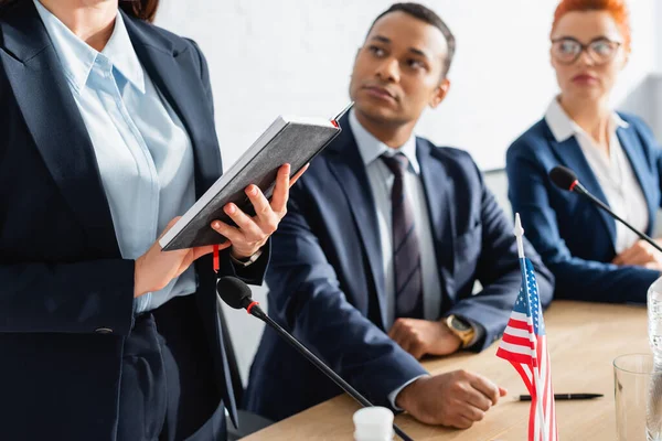 Politiker-Parteimitglieder blicken auf Kollegen, der mit Notizbuch im Sitzungssaal vor verschwommenem Hintergrund steht — Stockfoto