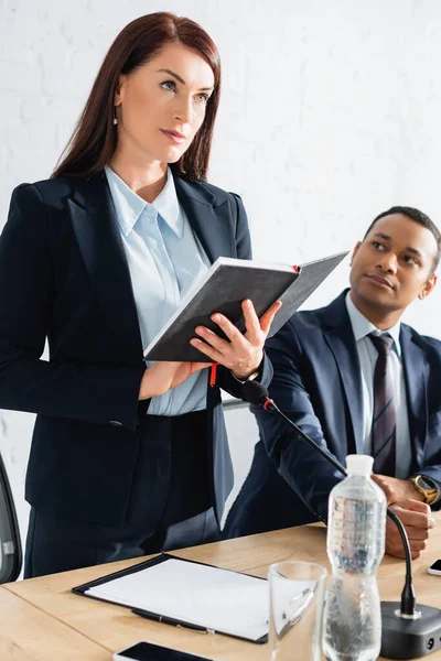 Confident female politician standing with notebook near indian colleague during political party meeting — Stock Photo