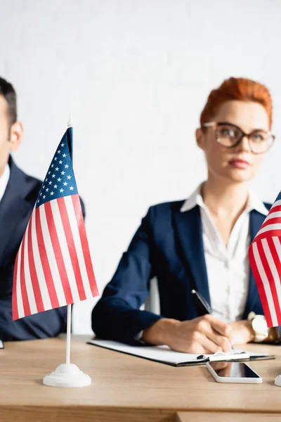 Banderas americanas pequeñas en la mesa con gente borrosa en el fondo - foto de stock