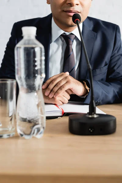 Cropped view of indian politician sitting near microphone with clenched hands on blurred foreground — Stock Photo