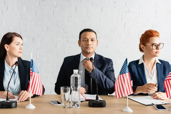 Confident indian politician touching tie, while sitting near colleagues during political party meeting — Stock Photo