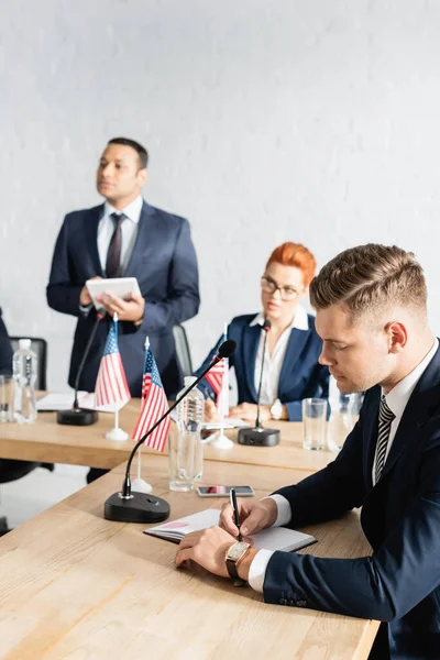 Politiker schreibt während des Parteitags in Notizbuch mit verschwommenen Personen im Hintergrund — Stockfoto