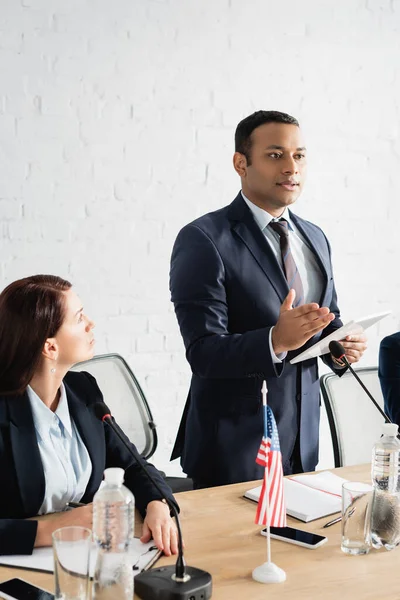 Donna politico guardando collega indiano che punta con mano, tenendo tablet digitale in sala riunioni — Foto stock