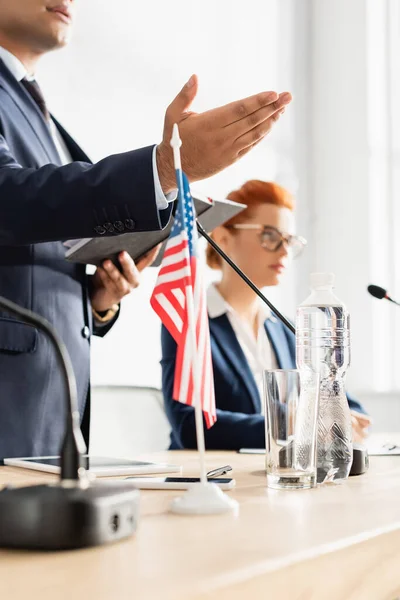 Indischer Politiker zeigt mit der Hand, während er ein Notizbuch während eines Parteitreffens mit einer verschwommenen Frau im Hintergrund hält — Stockfoto