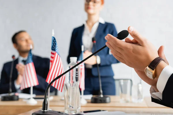Politician applauding sitting near microphone in boardroom with blurred colleagues on background — Stock Photo