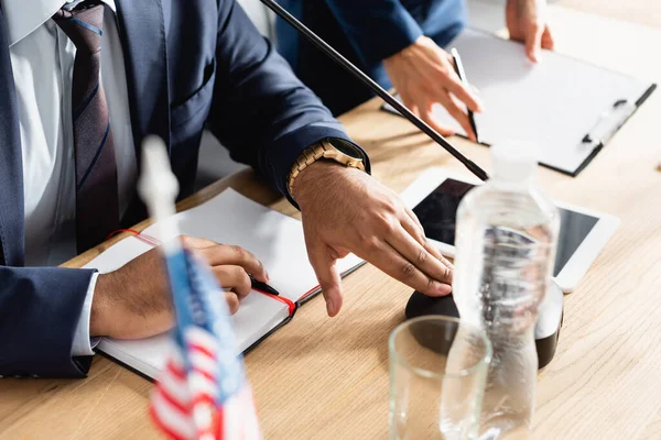 Vista ritagliata del politico indiano con penna vicino notebook vuoto, toccando il microfono in primo piano sfocato — Foto stock