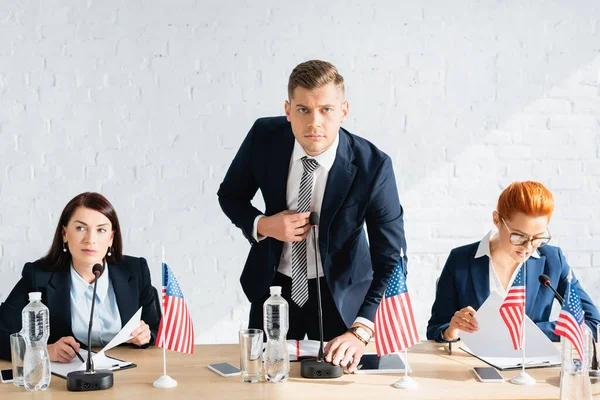 Mann in offizieller Kleidung blickt in die Kamera, während er sich im Sitzungssaal lehnt und das Mikrofon berührt — Stockfoto