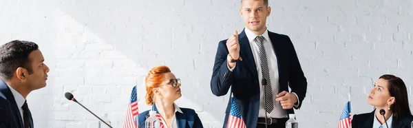 I politici interrazziali guardando collega fiducioso gesticolando e parlando durante la riunione del partito politico, banner — Foto stock