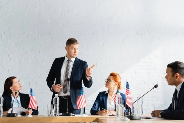 Serious politician pointing with finger while standing and looking at colleague during political party congress in boardroom — Stock Photo