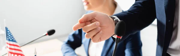 Cropped view of politician pointing with finger, while standing near microphone with blurred woman on background, banner — Stock Photo