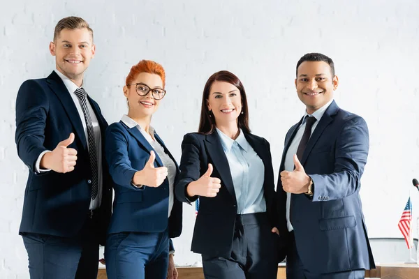 Lächelnde Multikulti-Politiker mit erhobenem Daumen, die im Sitzungssaal in die Kamera schauen — Stockfoto