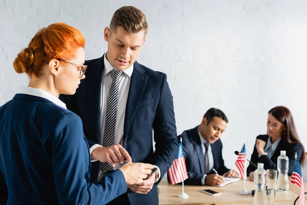 Man pointing with finger near colleague while party members working on blurred background — Stock Photo