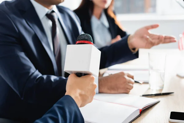 Vista ritagliata del giornalista con microfono intervistando politico durante la conferenza stampa su sfondo sfocato — Stock Photo