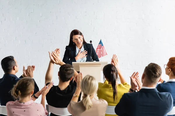 Grateful candidate holding hand on chest while standing in front of applauding voters in conference hall — Stock Photo
