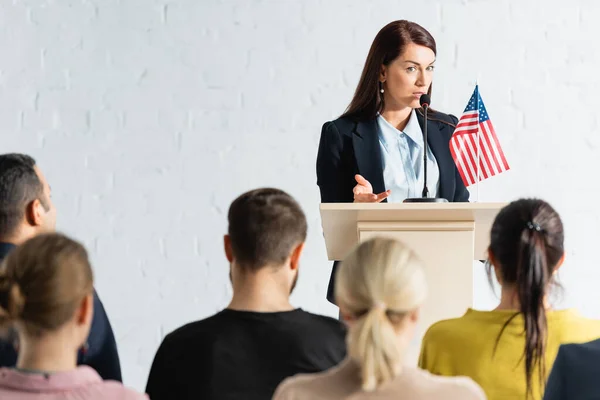 Political agitator talking to voters in conference hall on blurred foreground — Stock Photo