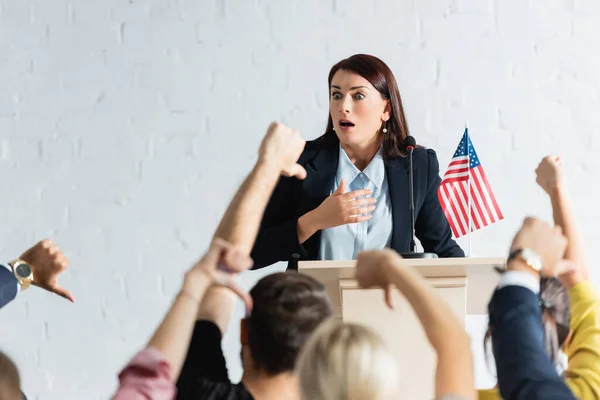 Conmocionado agitador político en frente de los votantes mostrando pulgares hacia abajo en la sala de conferencias, borrosa primer plano - foto de stock