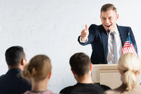 Excited political agitator pointing with finger at electors in conference hall, blurred foreground — Stock Photo