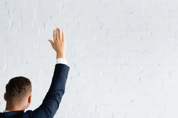 Вид сзади человека, голосующего с поднятой рукой против стены из белого брика — стоковое фото