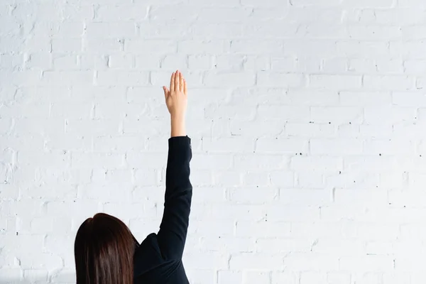 Вид ззаду жінки, що голосує з рукою в повітрі проти білої цегляної стіни — стокове фото