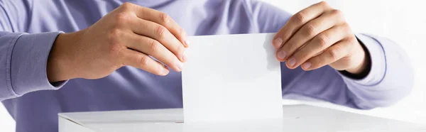 Vista recortada del hombre insertando papeleta en la urna electoral, pancarta - foto de stock