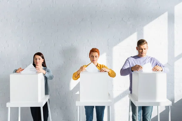 Votantes insertando papeletas en las urnas contra la pared de ladrillo blanco - foto de stock