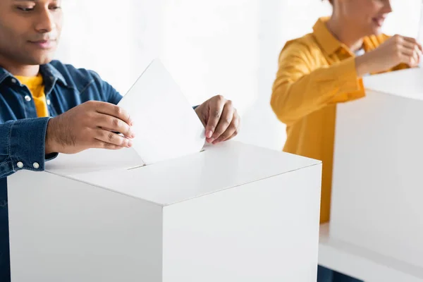 Uomo indiano inserimento scheda elettorale in polling box vicino donna su sfondo sfocato — Stock Photo