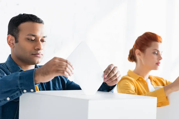 Multicultural electors inserting ballots into polling boxes on blurred background — Stock Photo