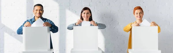 Multicultural electors inserting ballots into polling booths, banner — Stock Photo