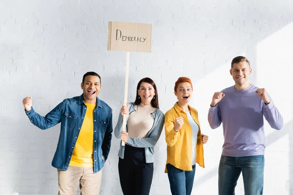 Woman holding placard with democracy lettering near excited multicultural like-minded people — Stock Photo
