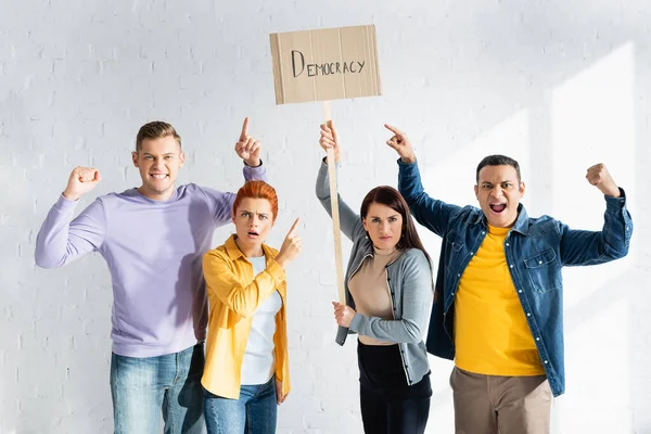 Personas multiculturales enojadas señalando con los dedos a la pancarta con letras de democracia - foto de stock