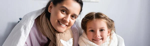 Mère malade et fille en écharpes souriant à la caméra sous couverture, bannière — Photo de stock