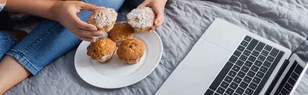 Teilansicht von Mutter und Tochter, wie sie Muffins vom Teller nehmen, während sie Film auf Laptop ansehen, Banner — Stockfoto