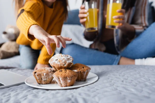 Vista ritagliata del bambino che prende muffin dal piatto vicino alla mamma con succo d'arancia su sfondo sfocato — Foto stock