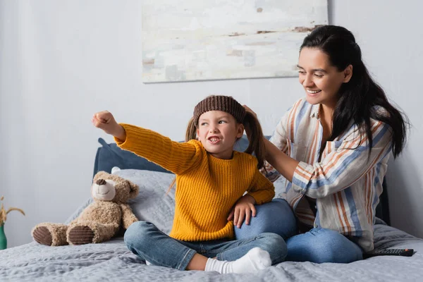 Aufgeregtes Mädchen im Stirnband grimmig mit ausgestreckter Hand neben lächelnder Mutter — Stockfoto