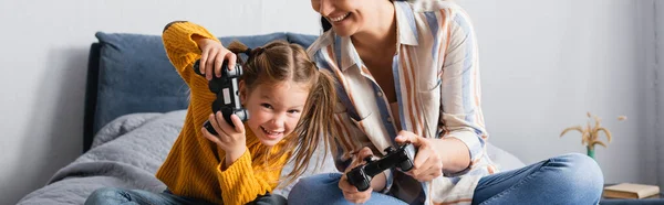 KYIV, UKRAINE - SEPTEMBER 15, 2020: excited woman and child playing video game in bedroom, banner — Stock Photo