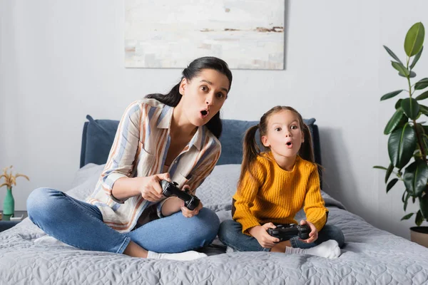 KYIV, UKRAINE - SEPTEMBER 15, 2020: shocked woman with daughter sitting with crossed legs and playing video game — Stock Photo