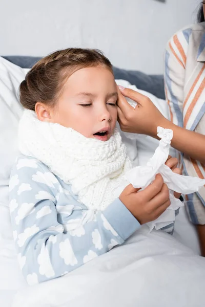Femme touchant enfant malade couché dans son lit et tenant des serviettes en papier — Photo de stock