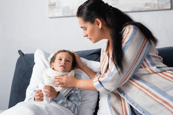 Diseased child lying in bed, holding paper napkin and looking at mother — Stock Photo