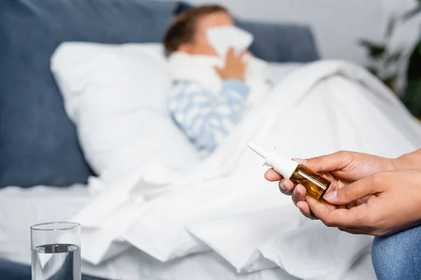 Woman holding nasal spray near sick daughter lying in bed on blurred background — Stock Photo
