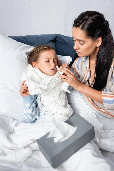 Mulher cura filha, sofrendo de corrimento nasal, com spray nasal — Fotografia de Stock